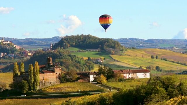 Hot air balloon flying over the castle of the Vault between hills with autumn colors in Barolo, Alba, Langhe, Piedmont, Italy