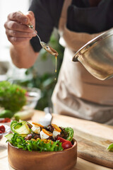 Close-up of chef adding soy sauce in dish with meat and vegetables at the table