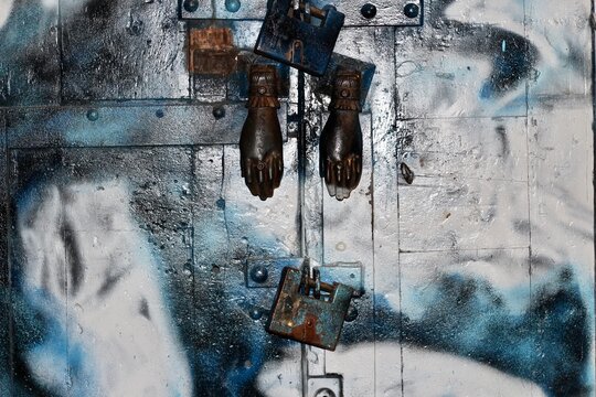 Puerta antigua pintada de blanco y azul. Cerrada con unos candados y con aldaba antigua en forma de mano