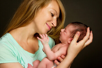 a young woman holds her newborn daughter in her arms. Studio photo on a black background.
