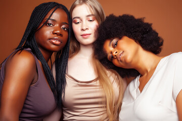 young pretty caucasian, afro, scandinavian woman posing cheerful together on brown background, lifestyle diverse nationality people concept