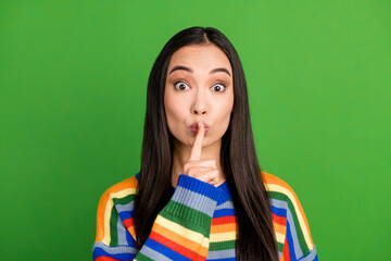 Close-up portrait of attractive mysterious girl showing shh sign keep silence isolated over bright green color background