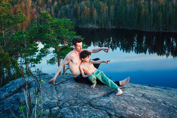 middle age man with little cute son doing sport yoga on the top of the mountain together, happy family lifestyle people outdoor, summer wild nature for training