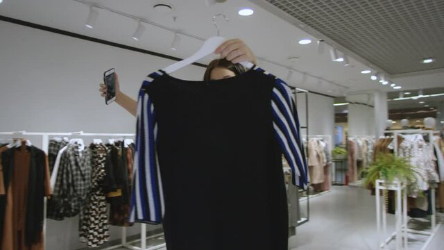 Attractive young woman dressed in red dress is taking a photo of herself with another dress, tracking shot, 360 degree