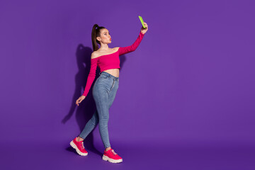 Full length photo of attractive lady hold telephone take selfie walk lips wear pink uncovered shoulders top isolated violet color background