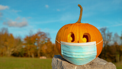 CLOSE UP, COPY SPACE Carved Halloween pumpkin wearing face mask covid protection