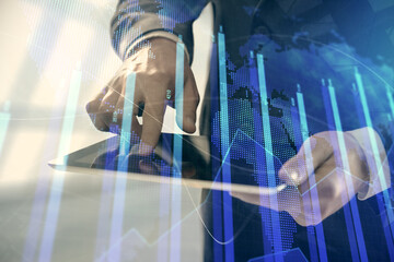 Double exposure of man's hands holding and using a digital device and forex graph drawing....