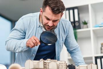 Architect male inspector examines a house model using a magnifying glass. House inspection and real estate concept.