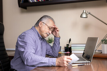 Senior man learn to use computer. Old man in glass and blue shirt Reads instructions for work using...