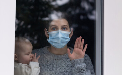 Young mother and daughter look out the window during a self-isolation quarantine