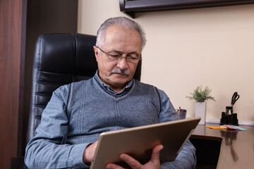 Senior man reading news on digital tablet. Senior man using tablet, sitting at desk at home. Modern technology, communication concept