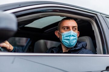young man in a medical mask driving a car.  crossing the quarantine zone by car. 
