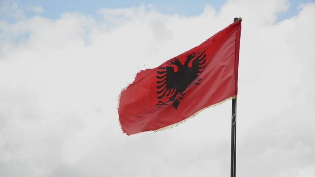 Albanian flag waving in the wind. Albanian national flag flying on a flagpole, against sky. State and national symbol. Shqipëri or Shqipëria. Red flag with black double-headed eagle.  Flamuri Kombëtar