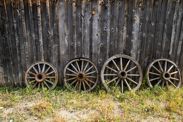 Fototapeta na wymiar Four wagon wheels against a wooden wall, with grass. Useful for rustic backgrounds