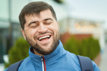 Bearded smiling cheeful young man walks outdoor in blue jacket.