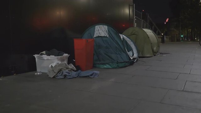 Two tents on a city sidewalk at night.