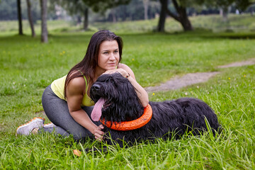 Woman hugs black briard during walking on open air in park.