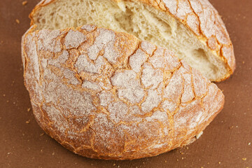 Round fresh white bread cut into two pieces is on a brown background