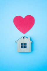 Love home, insurance and mortgage, marriage and valentine concept. Small wooden house toy and paper heart shape on blue background top view vertical