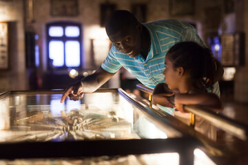 Afro father and his daughter looking at exhibits in glass stands at historical museum