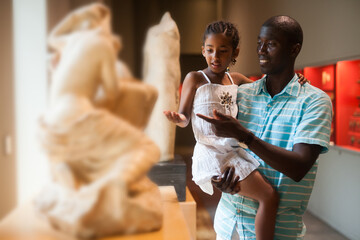 Afro man and his little daughter visiting exposition of Art Museum with exhibits of antiquity