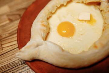 Top view on traditional Adjarian Khachapuri - open baked pie with melted salt cheese suluguni and egg yolk on wooden tray. Traditional georgian food
