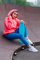 Stylish young woman sitting with her plastic skateboard in skatepark. Youth concept.