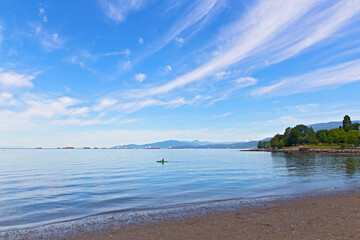 Panoramic view of English Bay with horizon over water and mountains, Vancouver, British Columbia, Canada. Kayak, seagulls, nautical vessels and snow mountain peaks in bay landscape on a sunny day.