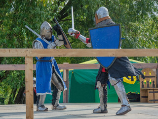 Two foot warriors in heavy medieval armor fight in the arena. Armed with swords. They are protected...