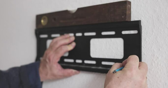man uses a spirit level to see if the television bracket is straight to drill it on the wall and draw the points on the wall