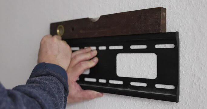 man uses a spirit level to see if the television bracket is straight to drill it on the wall and draw the points on the wall