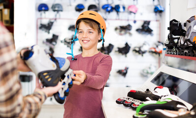 Fototapeta na wymiar Laughing male seller demonstrating roller-skates to boy customer in sports store.