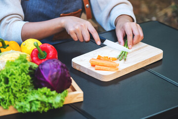 Closeup image of a woman cutting and chopping asparagus and carrot by knife on wooden board
