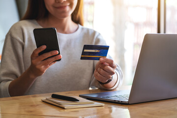 Closeup image of a woman holding credit card while using smart phone and laptop in office