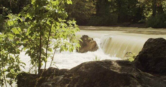 Side view of beautiful small rushing waterfall at flowing Eisbach river in the Englischer Garten on a german spring day, Munich, Slow motion