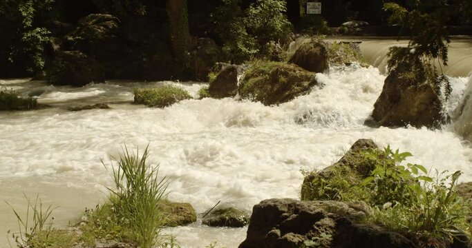 Beautiful small rushing waterfall at flowing Eisbach river in the Englischer Garten on a german spring day, Munich, Side view Slow motion