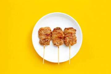 Grilled pork on white plate on yellow background.
