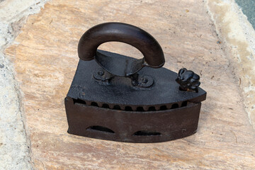 An antique cast rusted smoothing iron with a wooden handle working with coal of charcoal as a heat...