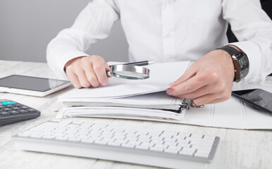 Man holding magnifying glass with documents.