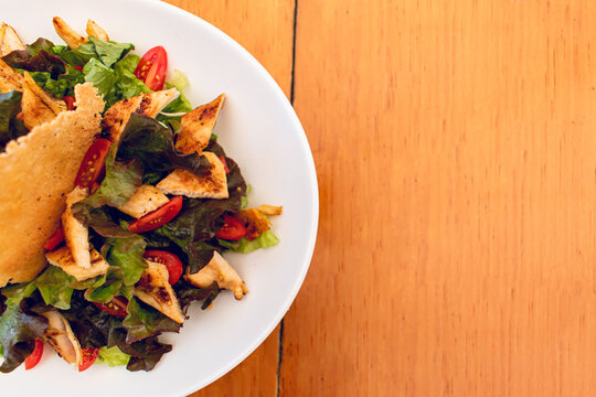 Plate of chicken salad with greens and vegetables on a wooden table