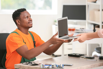 African-American technician giving fixed laptop to owner in service center