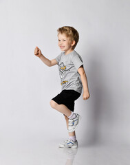 Cheerful frolic active blond kid boy in blue t-shirt and black shorts plays he is walking funny...