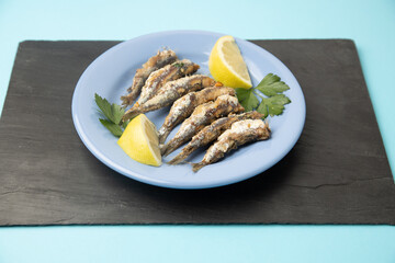 fried sardines, in blue plate with lemon wedge