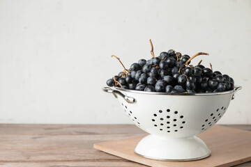 Colander with sweet ripe grapes on table