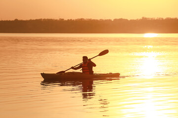Fototapeta na wymiar Young man kayaking in river at sunset