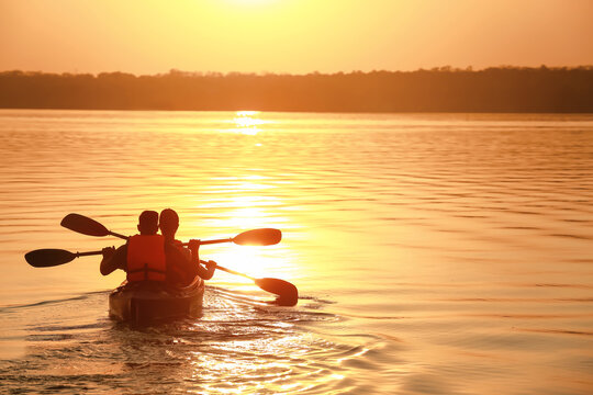 Young couple kayaking in river at sunset