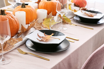 Beautiful table setting with pumpkins and autumn leaves in dining room