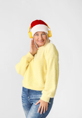 Mature woman listening to Christmas music on grey background