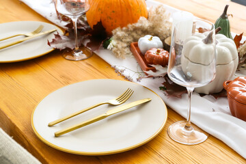 Beautiful table setting with pumpkins and autumn leaves in dining room