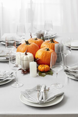 Beautiful table setting with pumpkins and autumn leaves in dining room